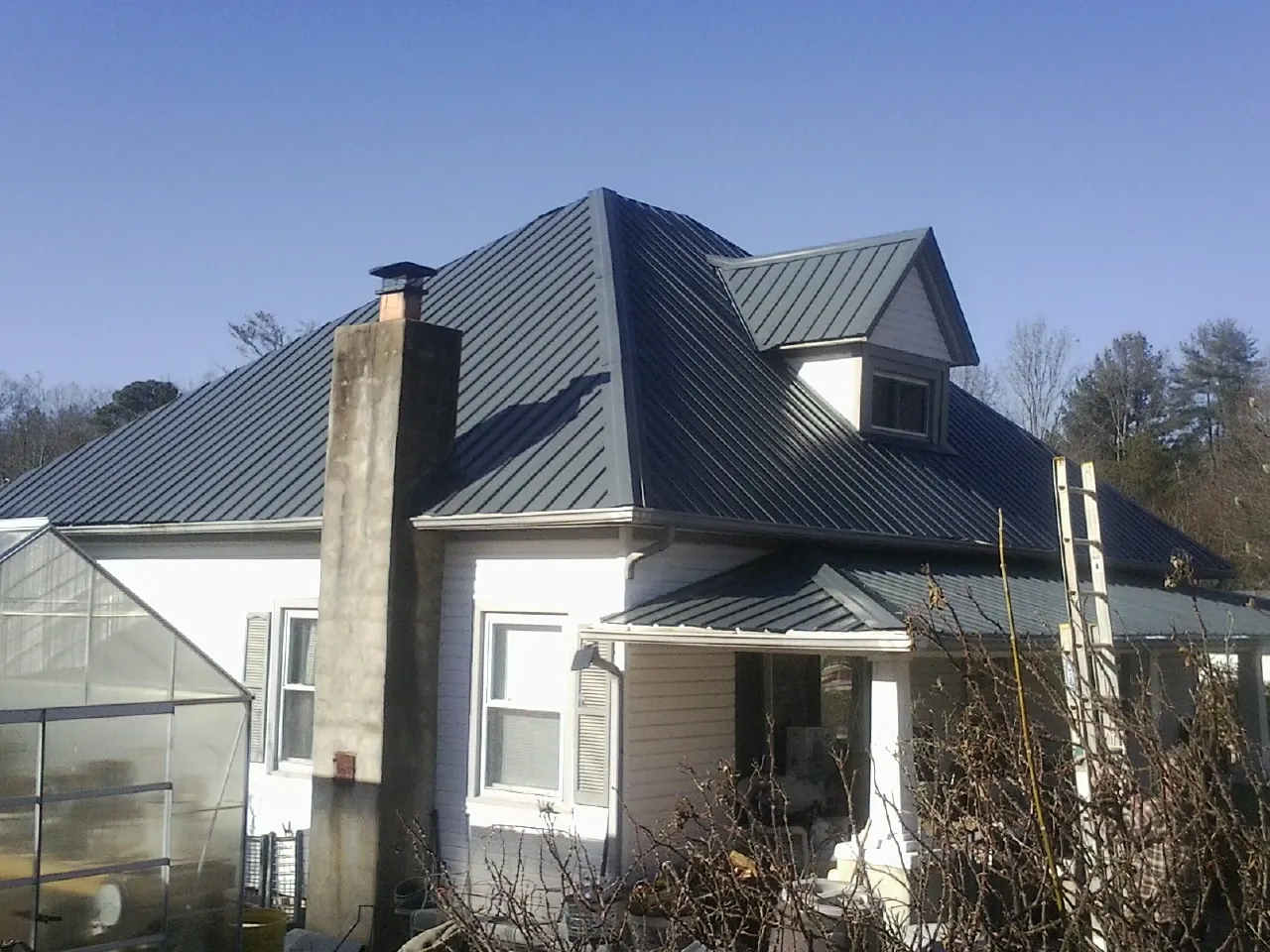 Dark blue standing seam metal roof on a white farmhouse with dormer — Slate & Tile Roof Repair by Roofing Brothers in Middlefield