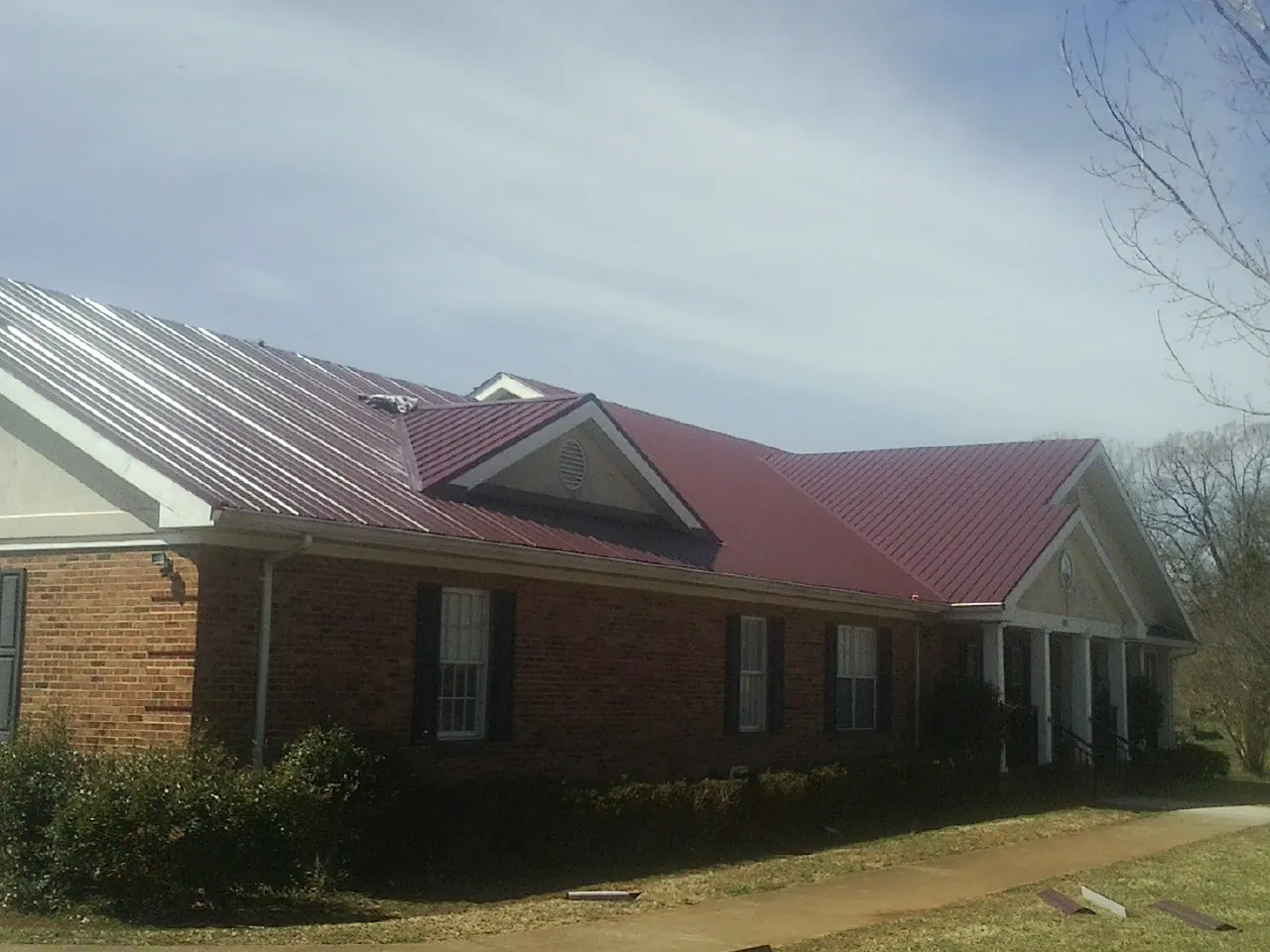 Red metal roof with gabled entries on a long brick building, from a Hail Damage Roof Repair job in Middlefield