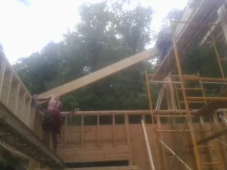Carpenter raising a rafter beam on a new second story frame in Middlefield