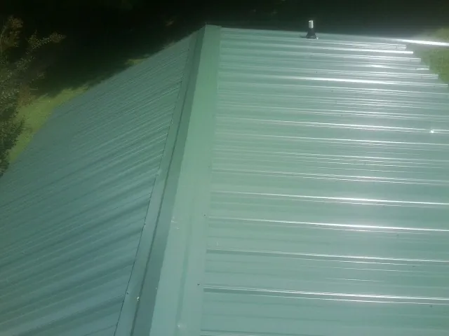 New green metal panels meeting at the ridge of a roof — Flat Roof Repair work by our crew in Middlefield