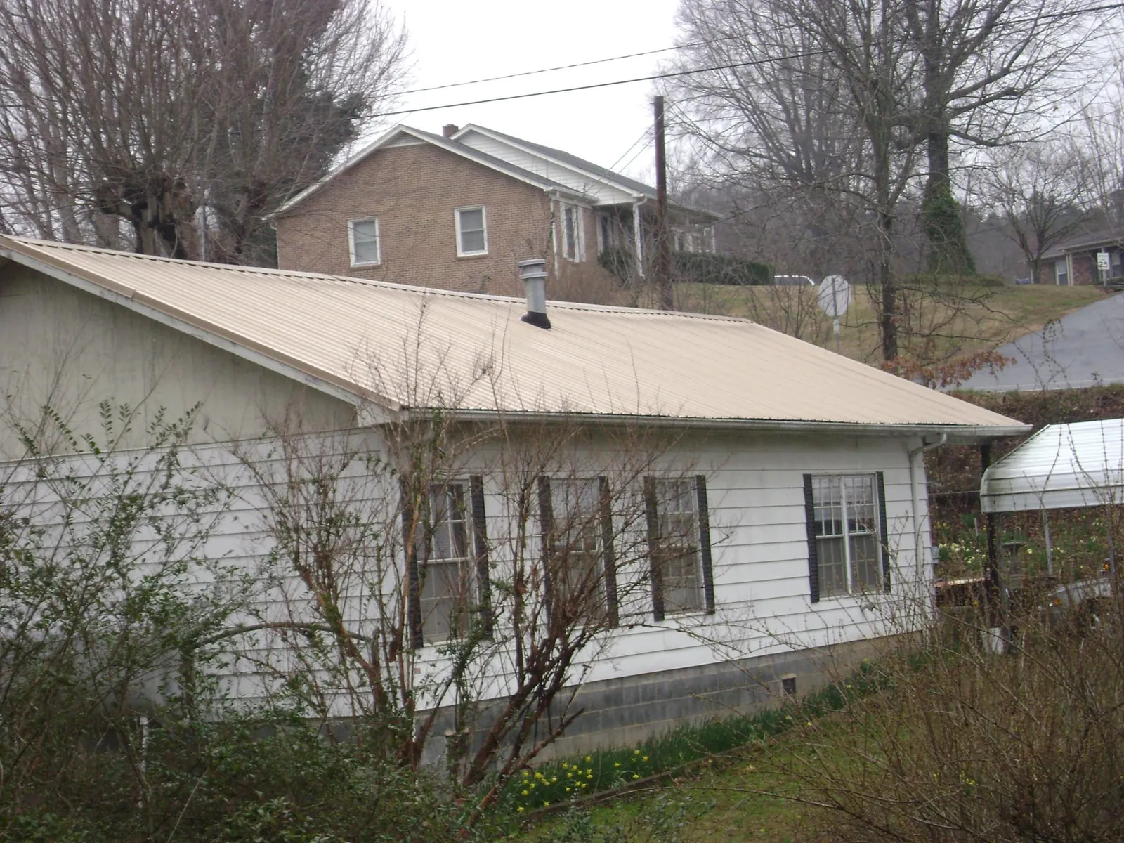 Tan metal roof on a white sided house set into a hillside — Commercial Roofing by Roofing Brothers in Middlefield